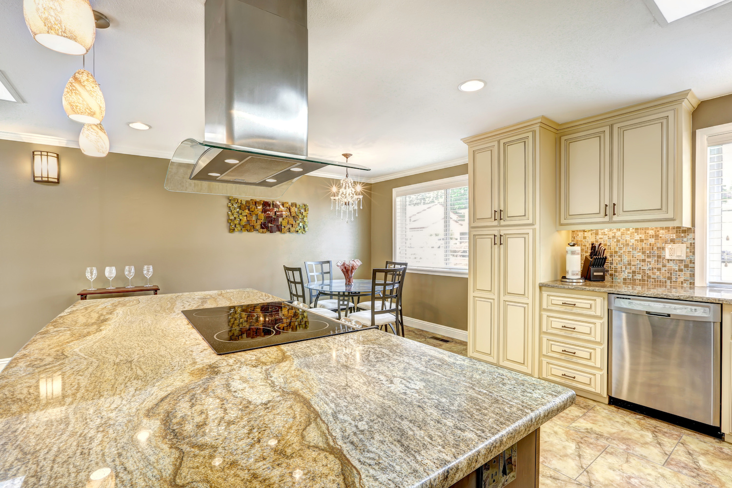 Spacious kitchen room with tile floor. Big kitchen island with built-in stove, granite top and steel hood